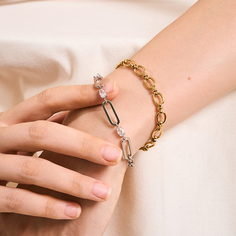 Gold chain bracelet with clear gemstones on a wrist against a beige background