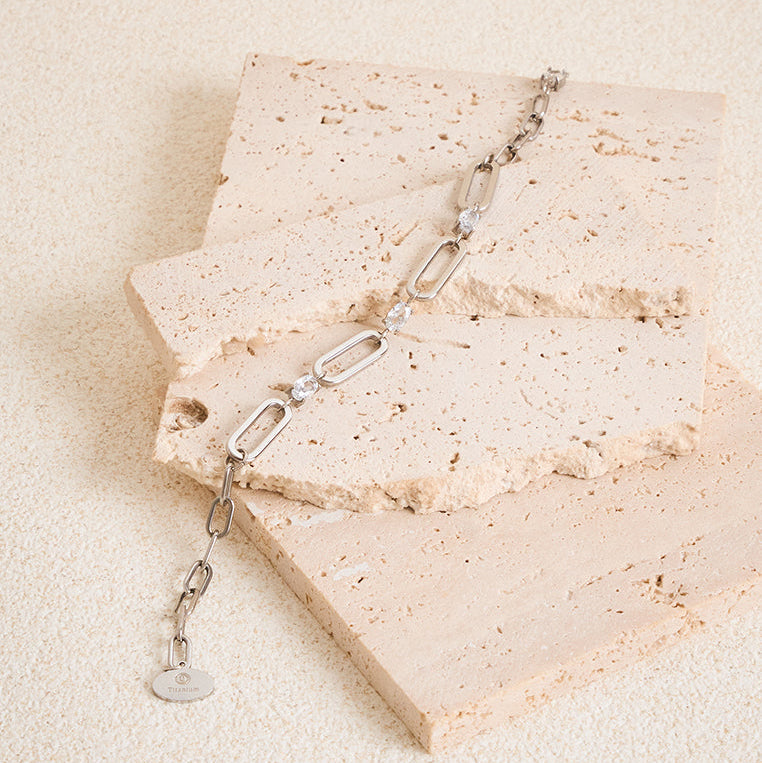 Silver chain necklace on a textured beige stone surface