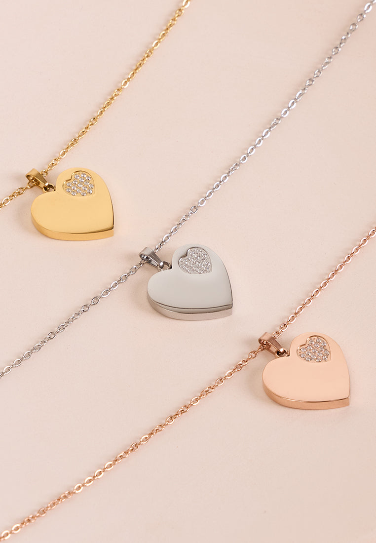 Three heart-shaped pendants on gold, silver, and rose gold chains against a beige background.